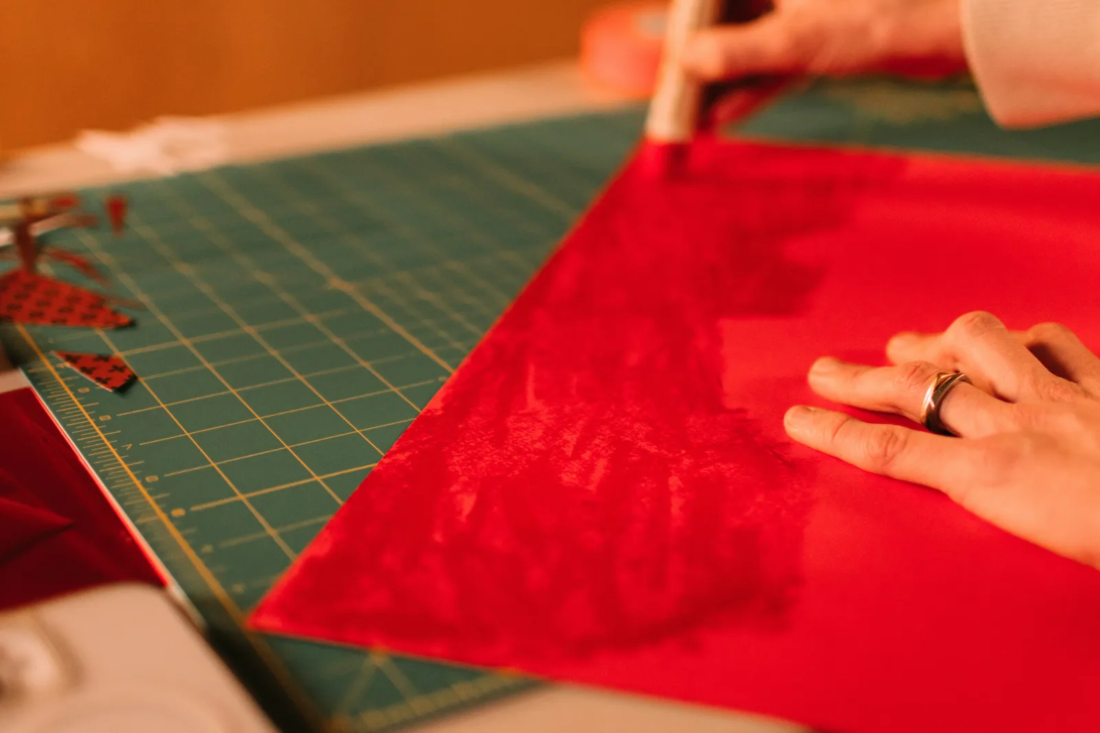 Close-up of two hands pressing a child's crayon drawing of the ocean onto a slightly larger piece of blue cardstock with a tape runner, a paper trimmer and scissors on the table, no faces, warm daylight