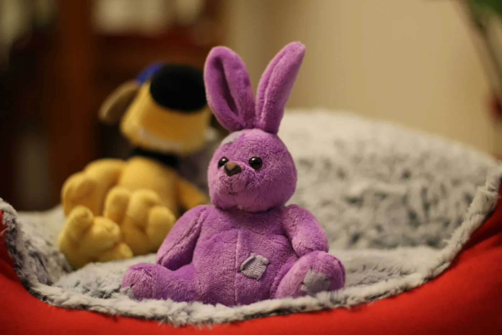 A child's hands holding a soft handmade plush of a lopsided orange creature, sitting on a bed with rumpled sheets, no face visible, warm morning light